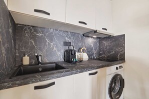 A modern kitchen with a marble countertop, a built-in washing machine, and a compact coffee maker. - Charming apartment - Center of Paris Montorgueil (Paris)