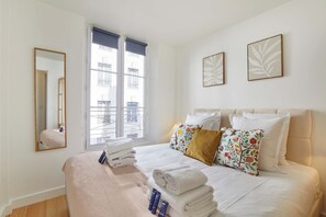 A hotel room with a bed, a window with blinds, a mirror, and two wall-mounted pictures. - Charming apartment - Center of Paris Montorgueil (Paris)