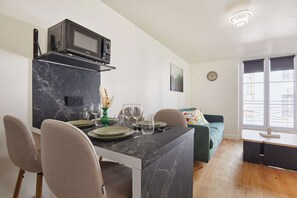 A modern kitchen with a built-in microwave, dining table set with plates and glasses, and a sofa in the adjacent living area. - Charming apartment - Center of Paris Montorgueil (Paris)