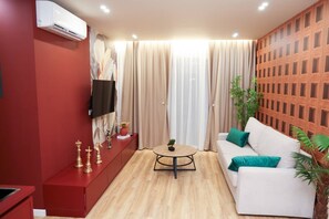 A modern living room with a red cabinet, a white sofa, a round coffee table, and a television mounted on the wall. - Altamar Luxury Suites Penthouse - 102 (Golem)