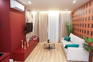 A modern living room with a red cabinet, a white sofa, a round coffee table, and a TV mounted on the wall. - Altamar Luxury Suites Penthouse - 102 (Golem)