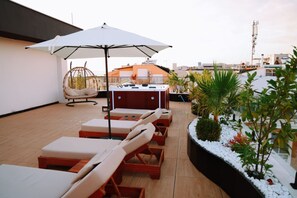 Eine Dachterrasse mit Liegestühlen, einer Hängematte, einem Grill und einem großen Sonnenschirm, der Schatten spendet.