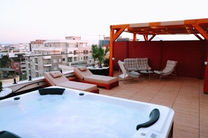 Eine Dachterrasse mit Whirlpool, Liegestühlen und einer Pergola.