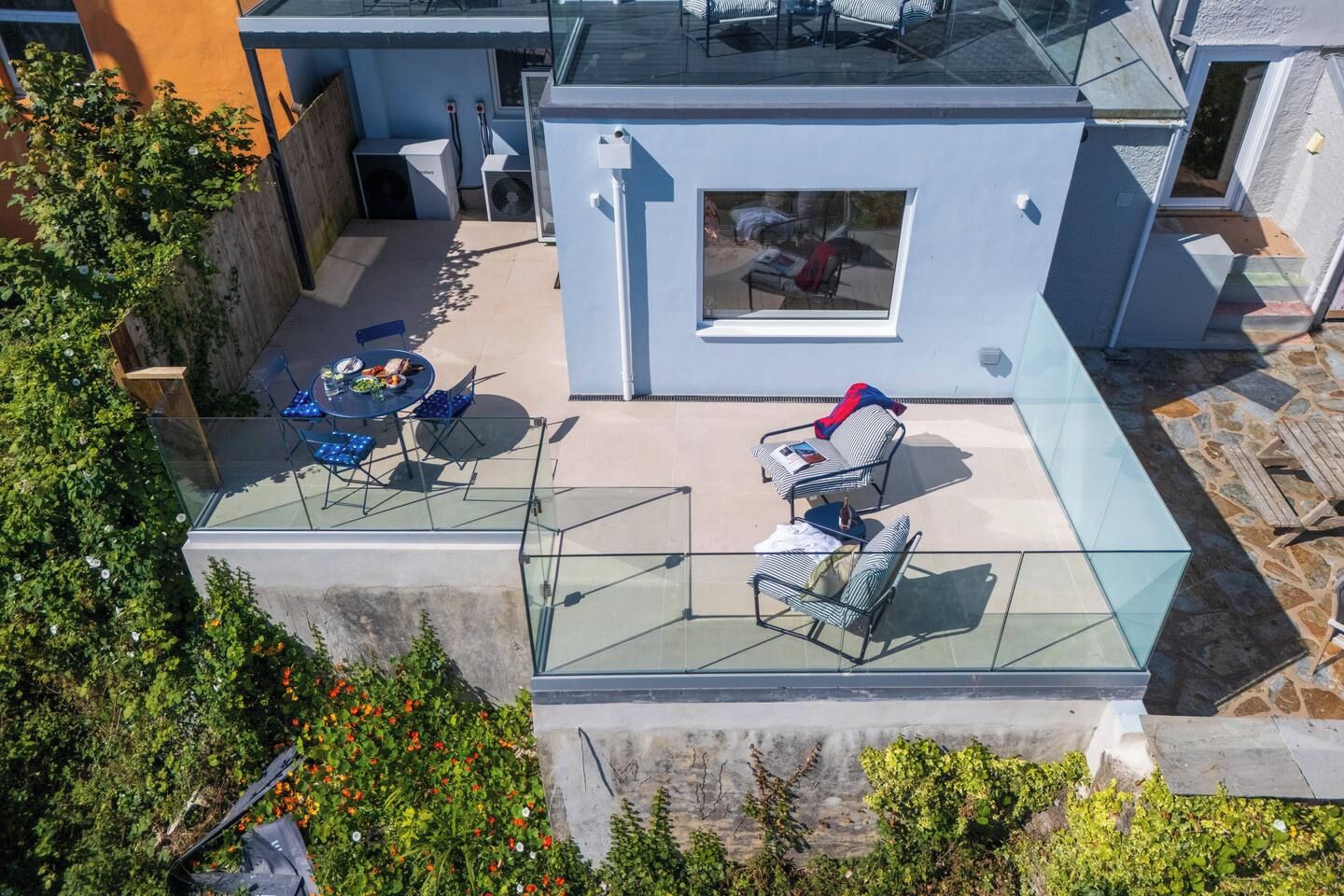 Une terrasse sur le toit dotée d’une balustrade en verre, d’un espace salon extérieur et d’un petit espace clos avec une fenêtre.