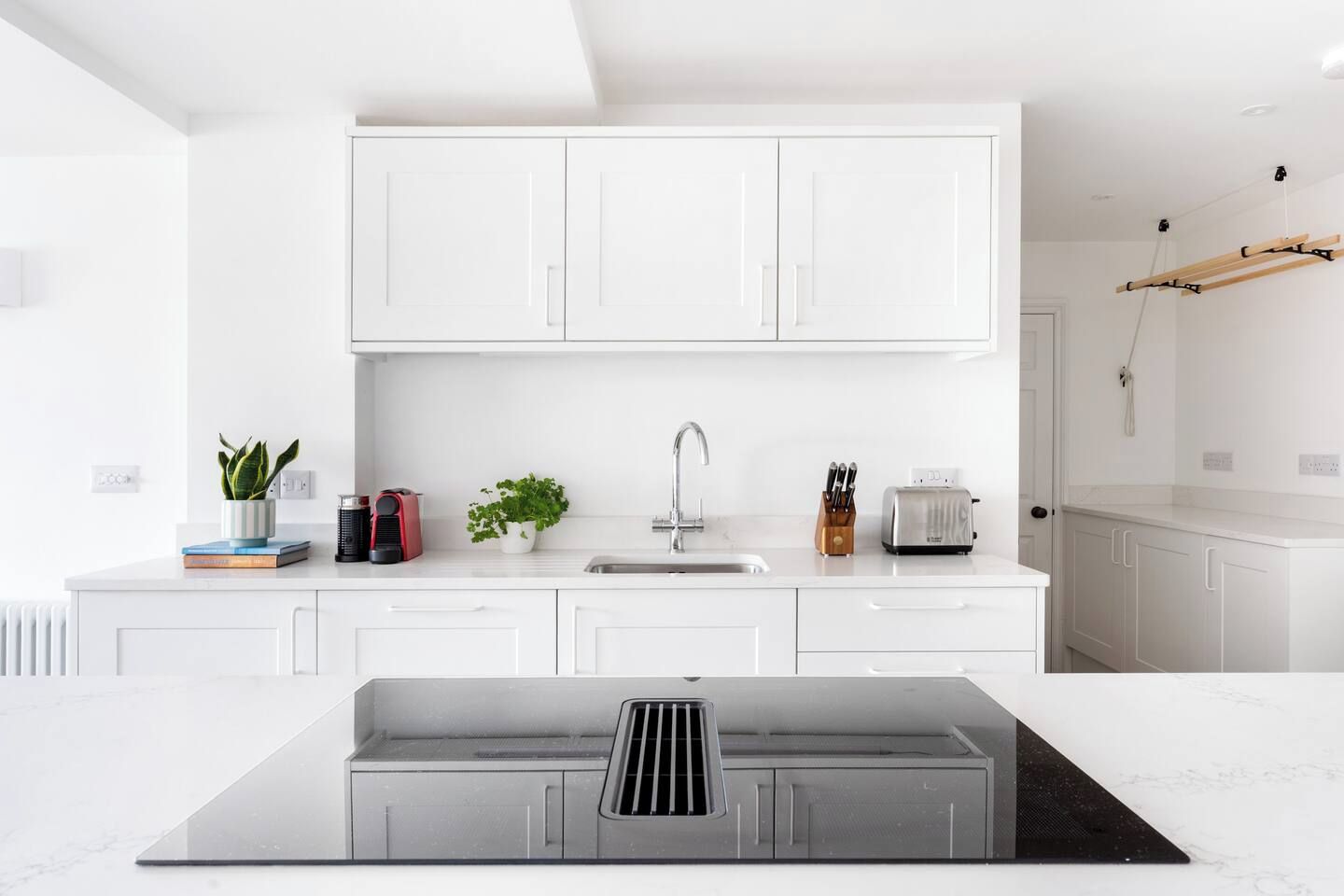 Une cuisine moderne avec des meubles blancs, un évier en acier inoxydable et une cuisinière encastrée.