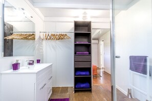 A modern bathroom with a white vanity, a mirror, and a built-in shelf unit with purple towels. - Sea-view villa in Tartane, sleeps 8 & spa (La Trinité)