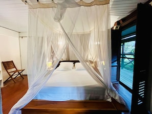 A room with a bed under a canopy, a wooden bench, and a window with blinds. - Sea-view villa in Tartane, sleeps 8 & spa (La Trinité)
