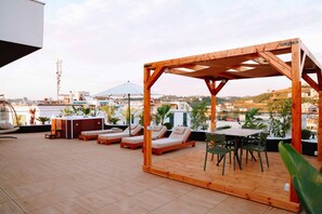 A rooftop terrace with wooden pergola, lounge chairs, a table with chairs, and potted plants. - Altamar Luxury Suites Penthouse - 101 (Golem)