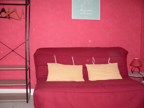 A red bed with two pillows and a metal shelf unit against a pink wall. - Country house 'Gîte Clos Saint Vincent' with Wi-Fi (Verdigny)