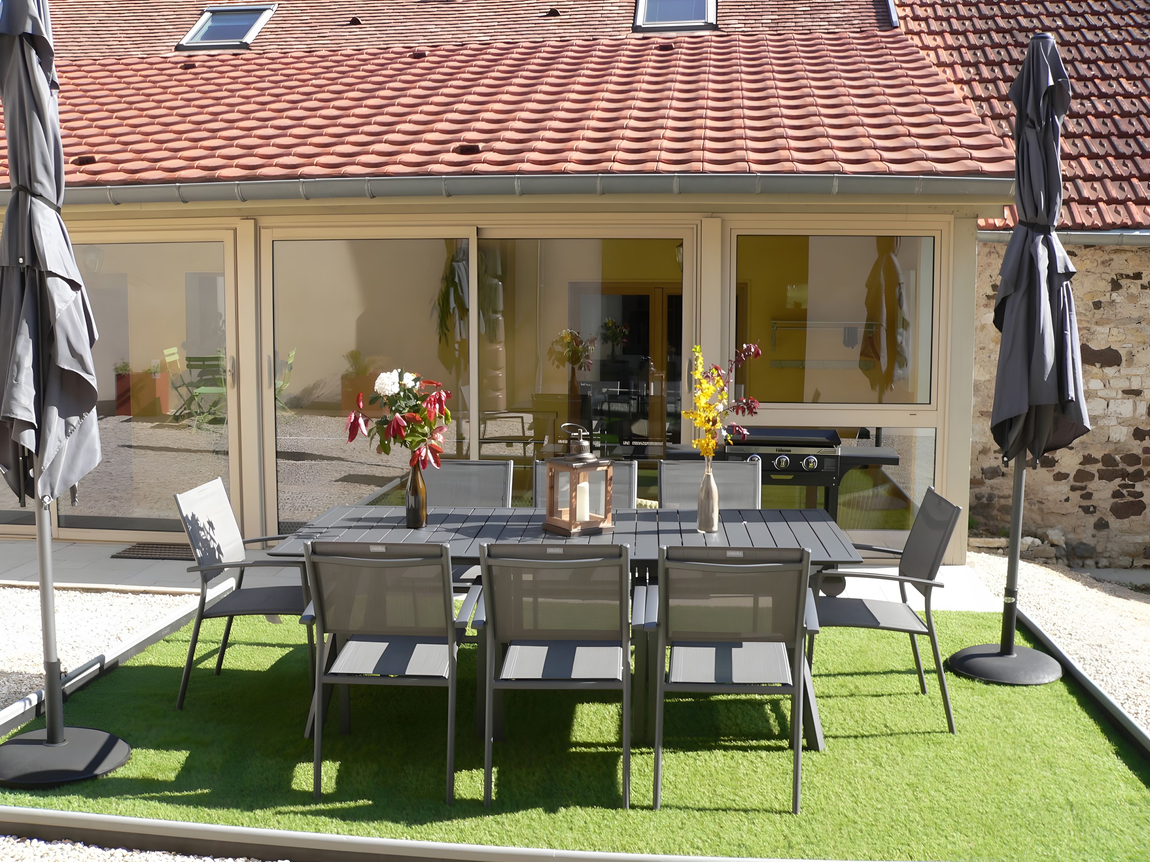 Eine Terrasse im Freien mit Tisch, Stühlen, einem Grill und Sonnenschirmen.
