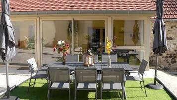 An outdoor patio with a table and chairs, a grill, and umbrellas.