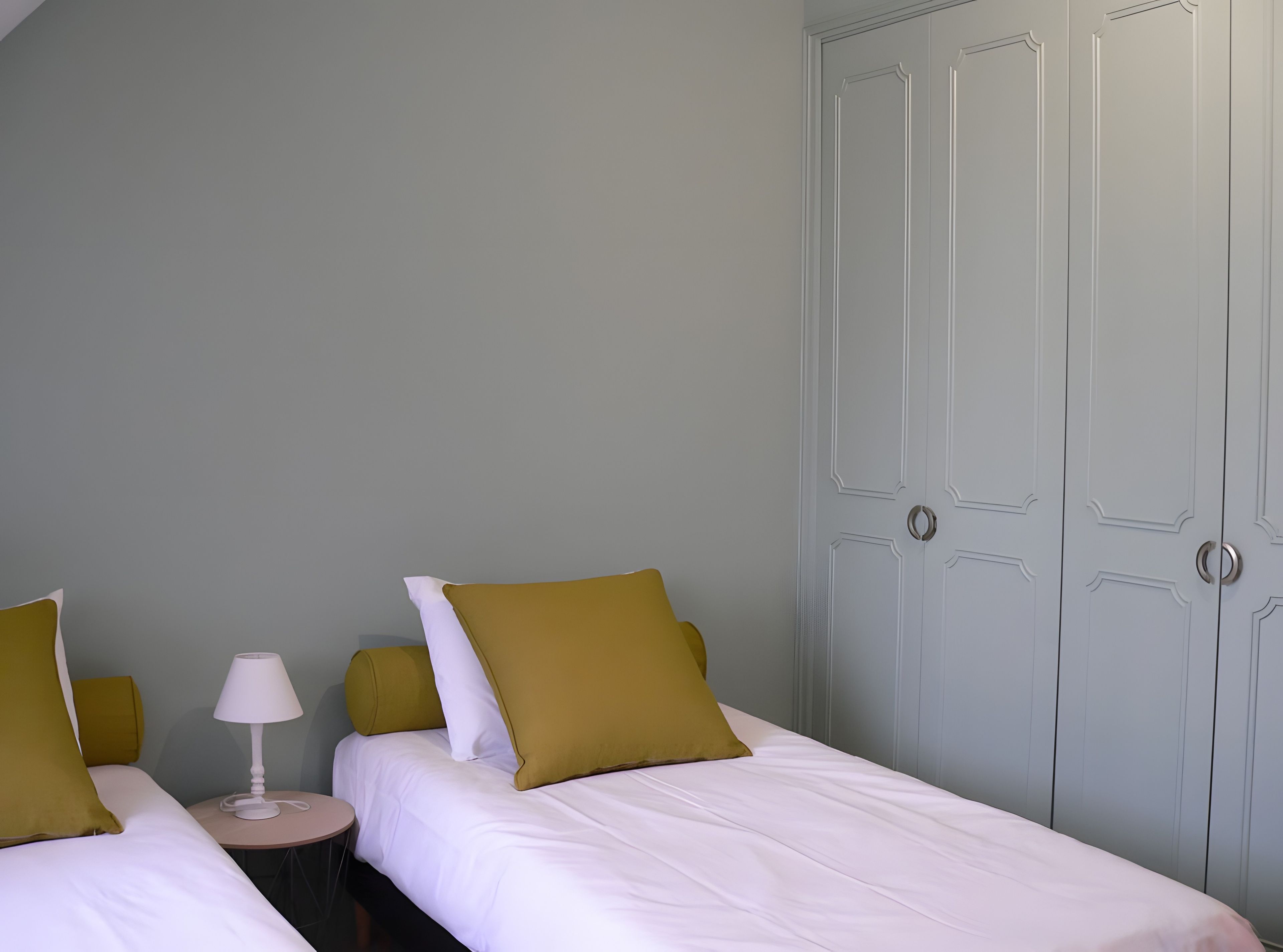 Hotellihuone, jossa on kaksi sänkyä, yöpöytä lampun kanssa ja vaatekaappi.