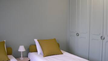 Hotellihuone, jossa on kaksi sänkyä, yöpöytä lampun kanssa ja vaatekaappi.