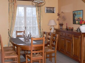 Un comedor con una mesa redonda, sillas, un centro de mesa de vidrio decorativo, una lámpara y un aparador con un jarrón de flores.
