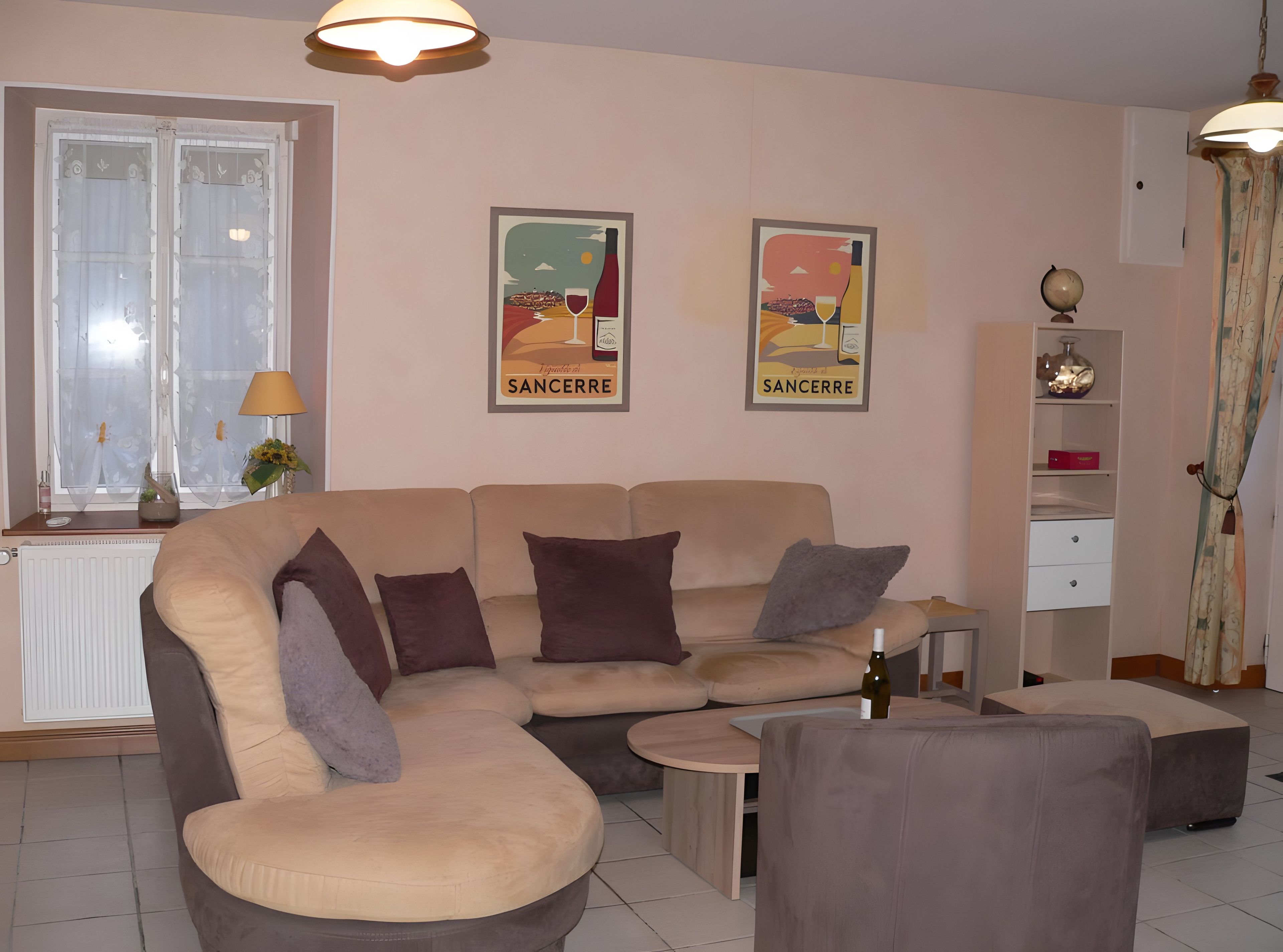 Een woonkamer met een beige bank, een kleine ronde tafel en twee posters aan de muur.