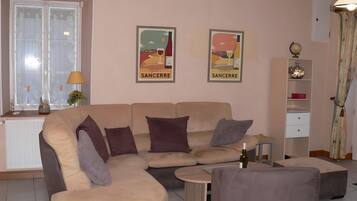 Een woonkamer met een beige bank, een kleine ronde tafel en twee posters aan de muur.