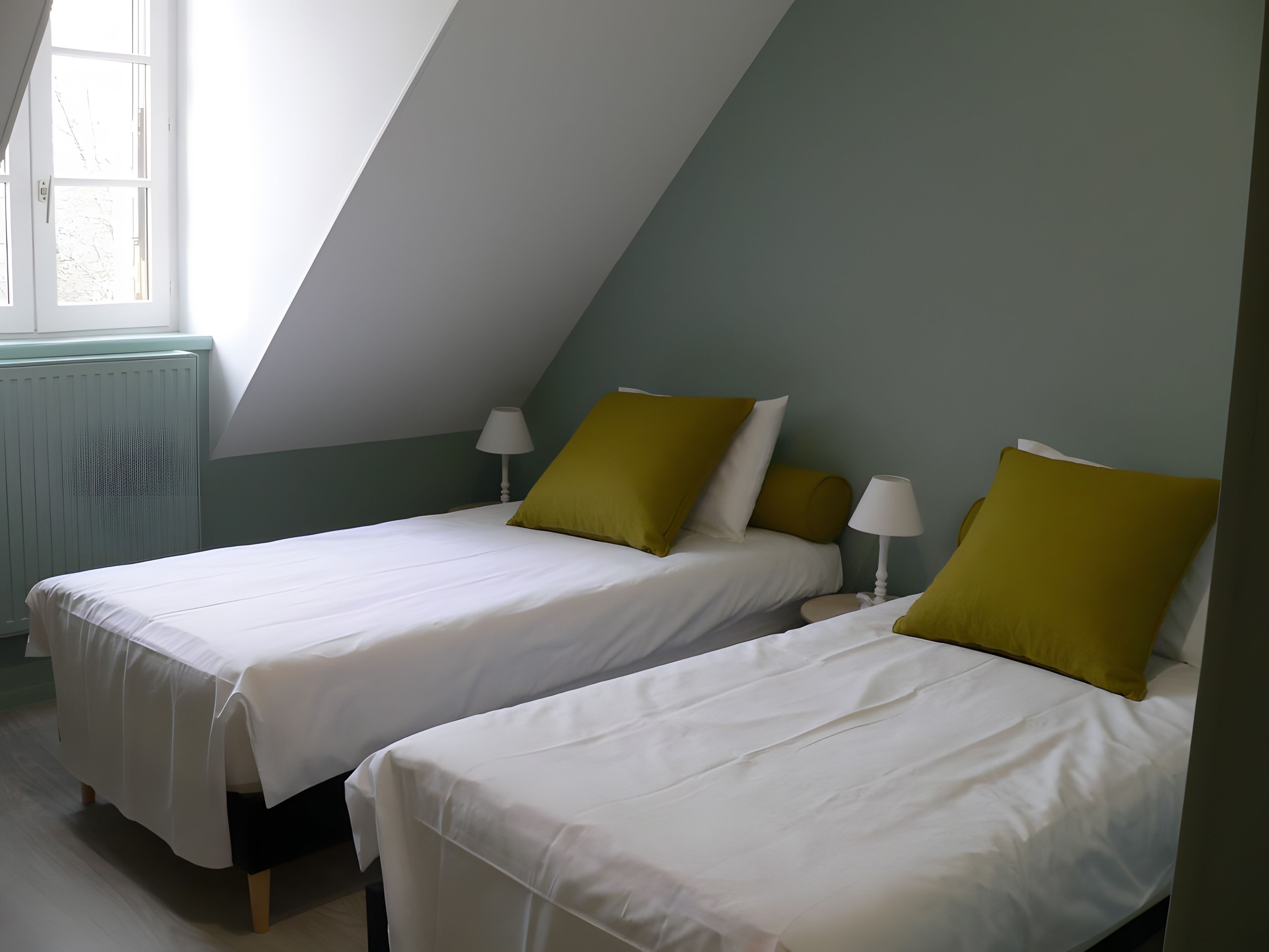 Ein Zimmer mit zwei Betten, jeweils mit weißer Bettwäsche und grünen Kissen, einem Fenster mit Ausblick und einer Heizung.