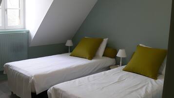 A room with two beds, each with white bedding and green pillows, a window with a view, and a radiator.