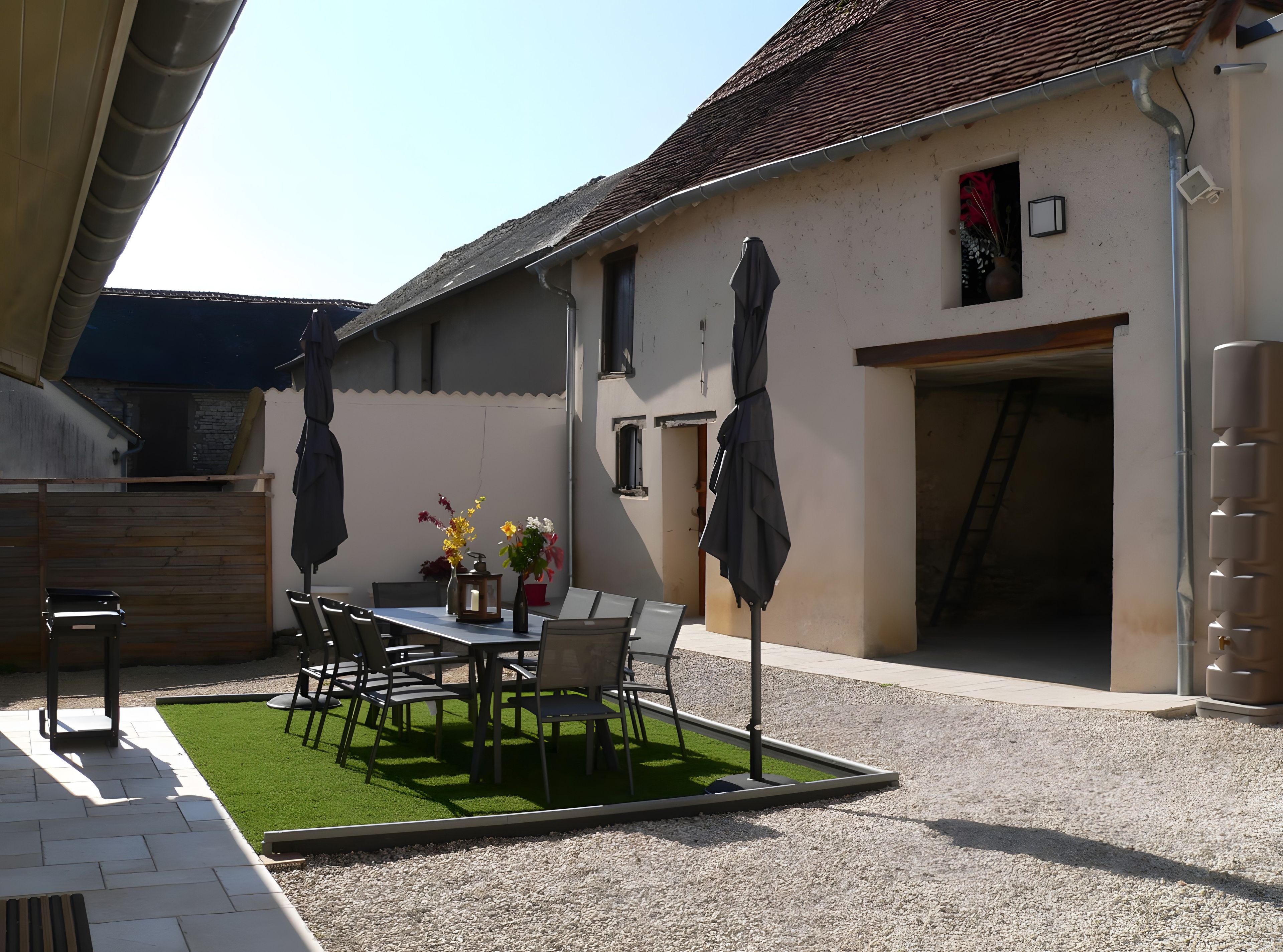 Eine Außenpatio mit Tisch und Stühlen, umgeben von Kies und einer kleinen Fläche mit Kunstrasen.