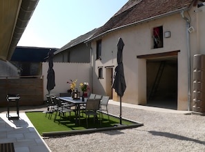 Un patio al aire libre con una mesa y sillas, rodeado de grava y una pequeña zona de césped artificial.
