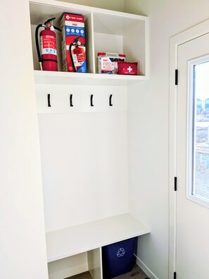 A white storage unit with hooks, a fire extinguisher, and a first aid kit.