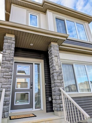 A multi-story residential building with a stone facade, a dark front door, and a welcoming mat.