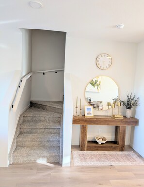 Una escalera que lleva a un rellano con una consola de madera, un espejo redondo y un reloj de pared.