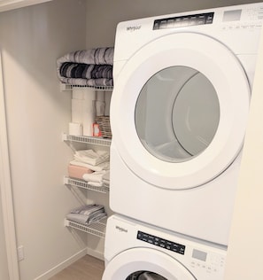 A stacked washer and dryer unit with a control panel and a shelf above holding folded towels.