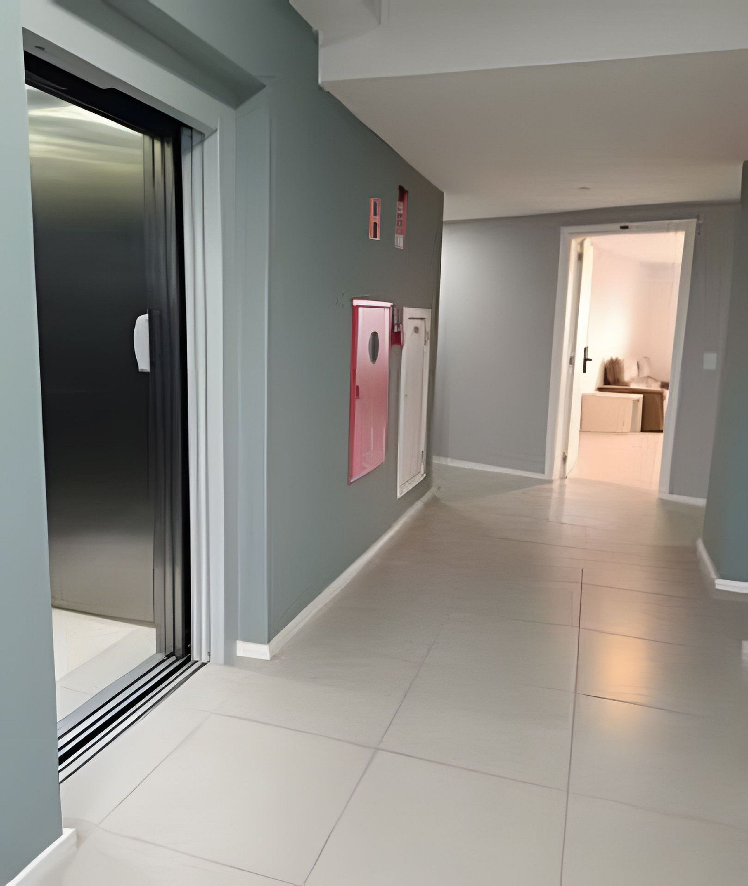 A hallway with a door on the left, a light switch on the wall, and a door on the right.