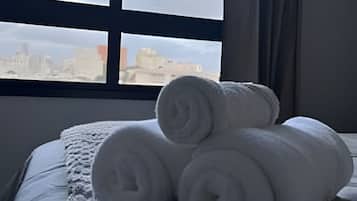 A bed with rolled white towels and a window with a city view.