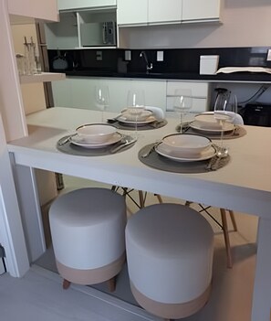Una cocina moderna con armarios blancos, encimera negra y una mesa de comedor con platos y vasos.