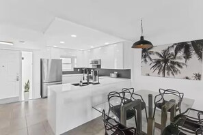 A modern kitchen with a central island, stainless steel appliances, and a dining area with chairs. - Emerald Isle 612 (Fort Walton Beach)