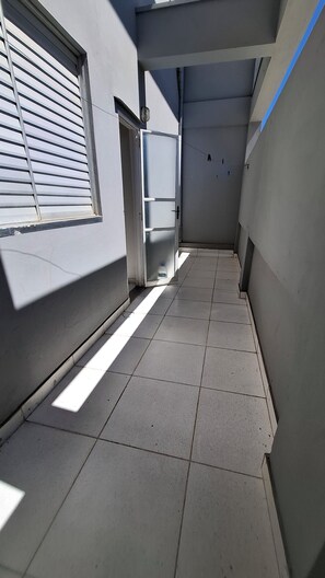 Un estrecho pasillo con piso de baldosas, una puerta que da a una habitación y una ventana con persianas.