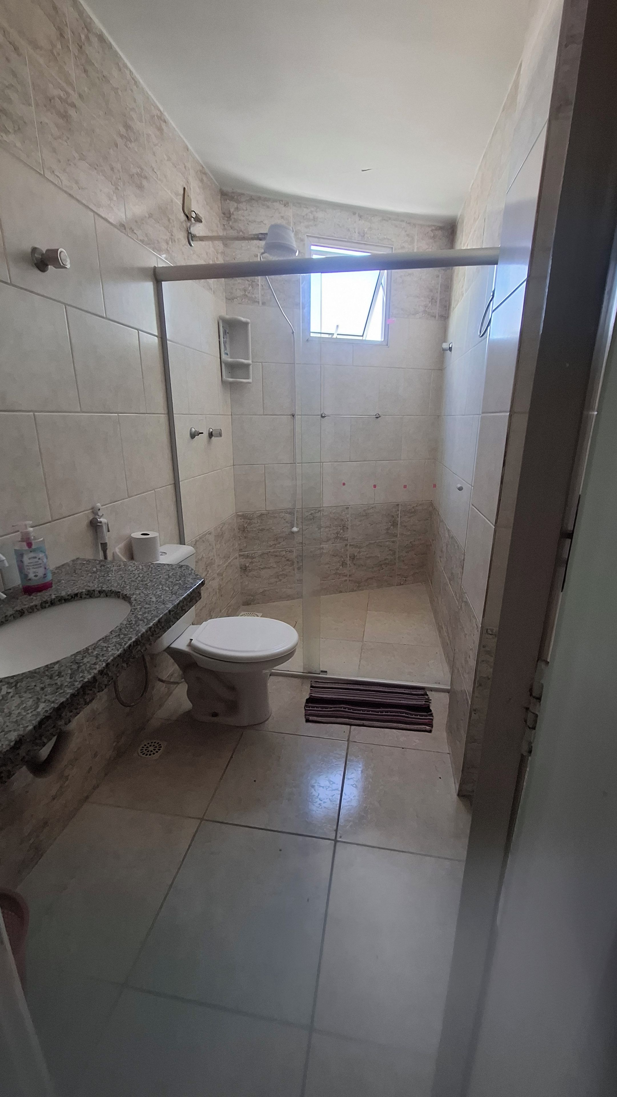 Un baño con inodoro, lavamanos, ducha y un ventanal pequeño.
