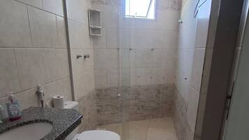 Un baño con inodoro, lavamanos, ducha y un ventanal pequeño.