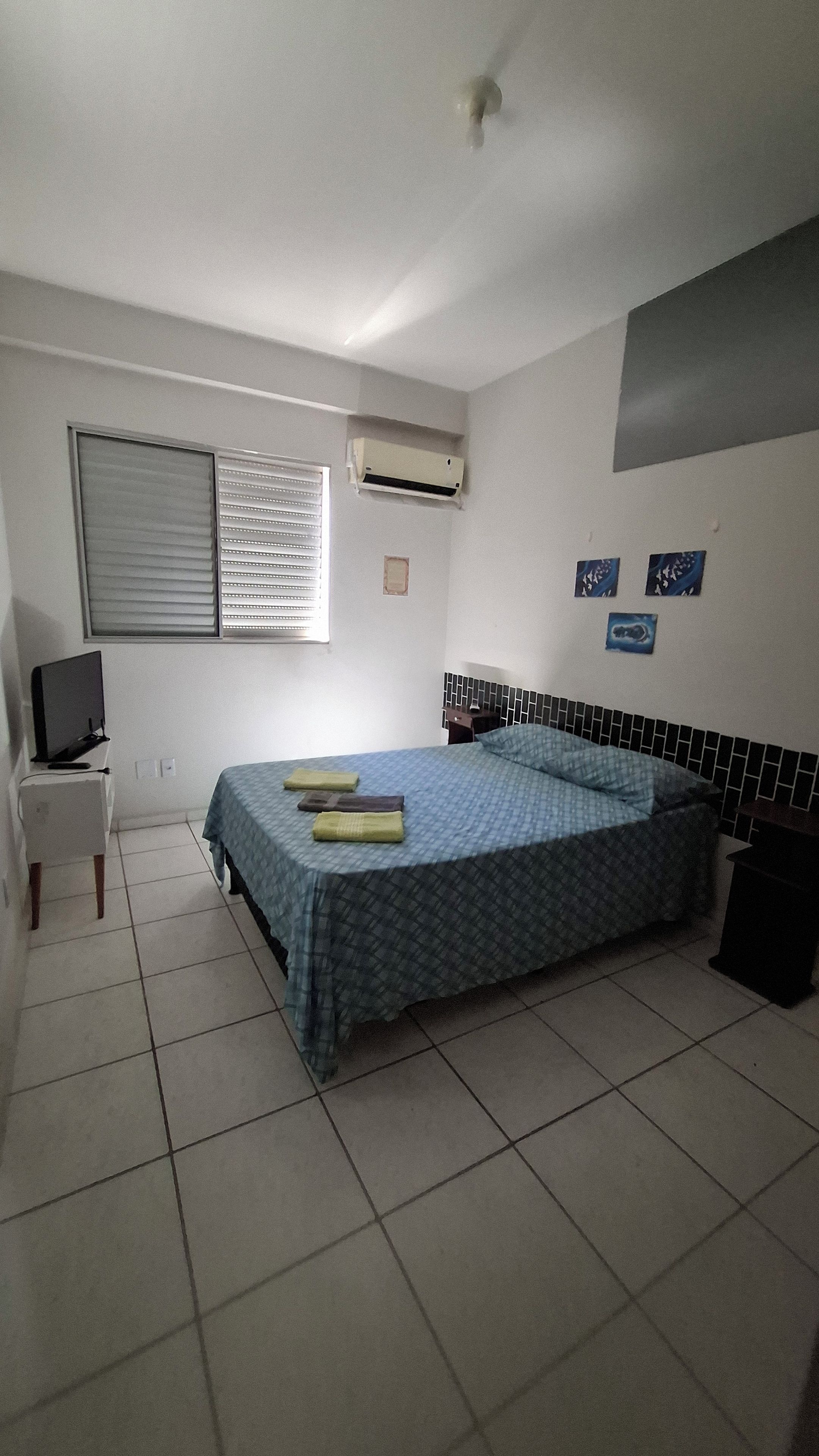 Un dormitorio con una cama, televisión, mesita de noche y aire acondicionado.