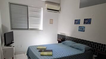 Un dormitorio con una cama, televisión, mesita de noche y aire acondicionado.