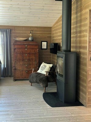 A cozy room with a wooden interior, a fireplace, a dresser, a chair, and a television. - Mountain cabin in Peer Gynt country, ski-in/out (Sør-Fron)