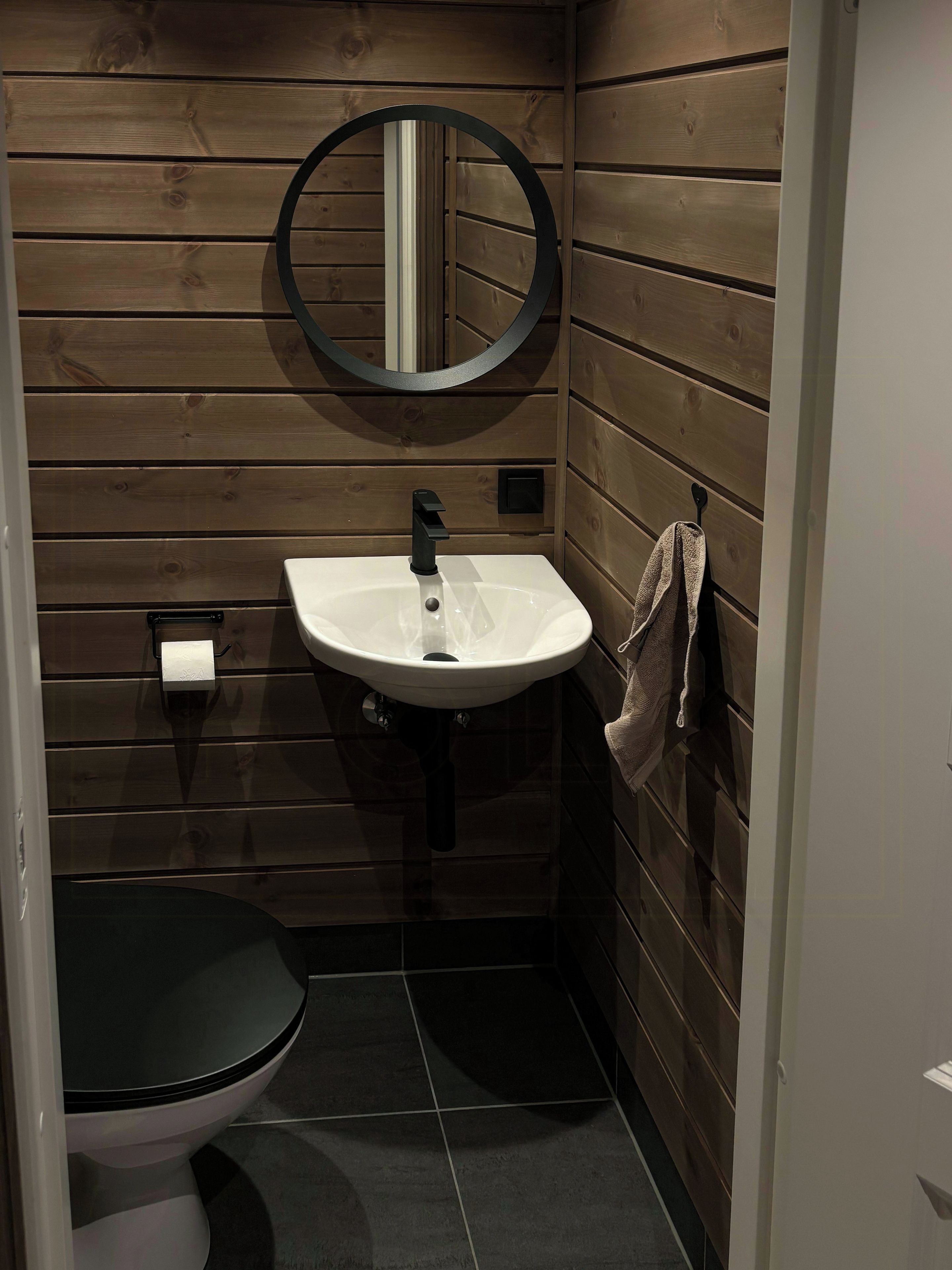 A compact bathroom with a white sink, black faucet, and a round mirror on the wall.