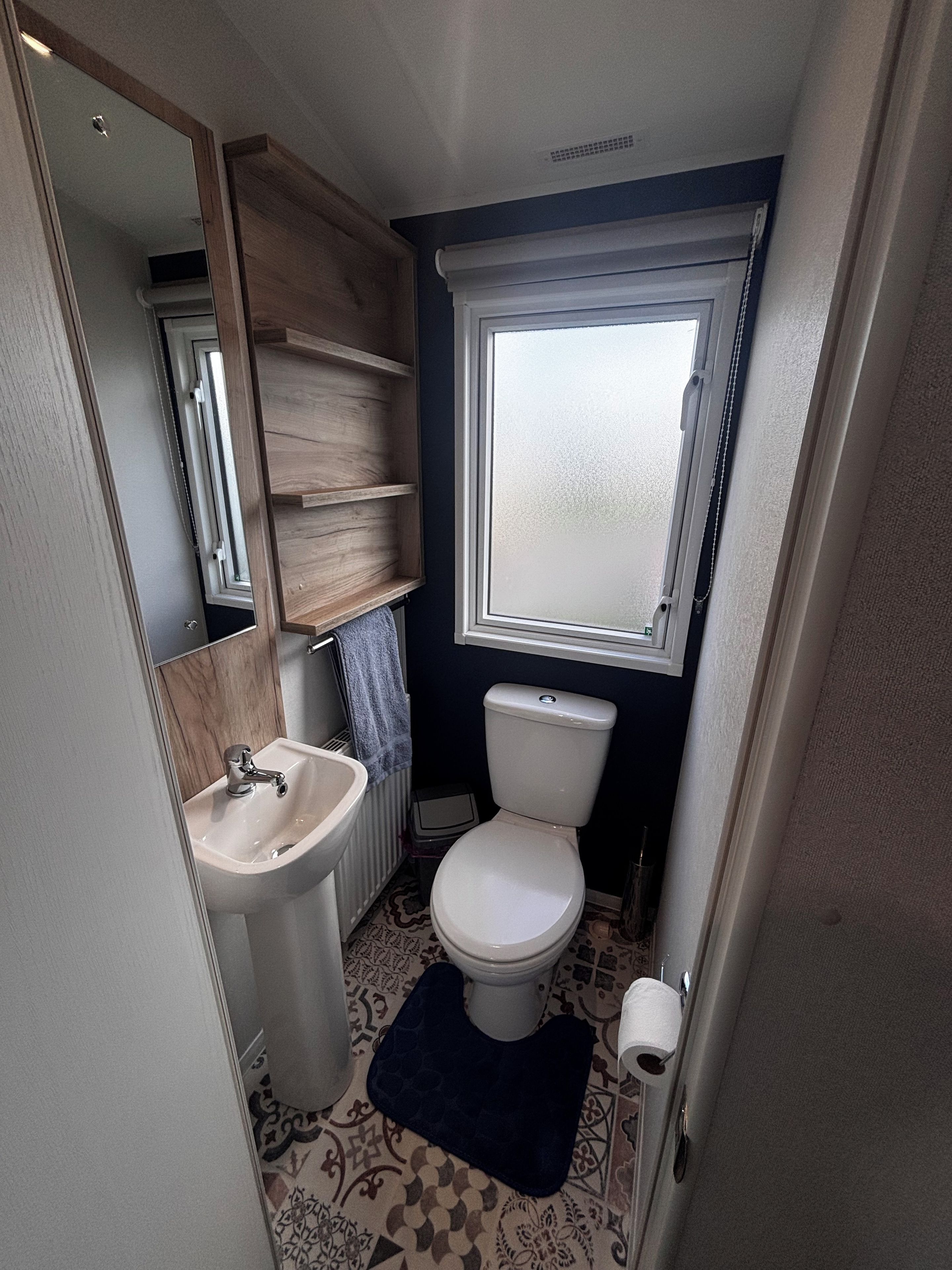 Un baño pequeño con lavamanos, inodoro y ventana sobre el inodoro.