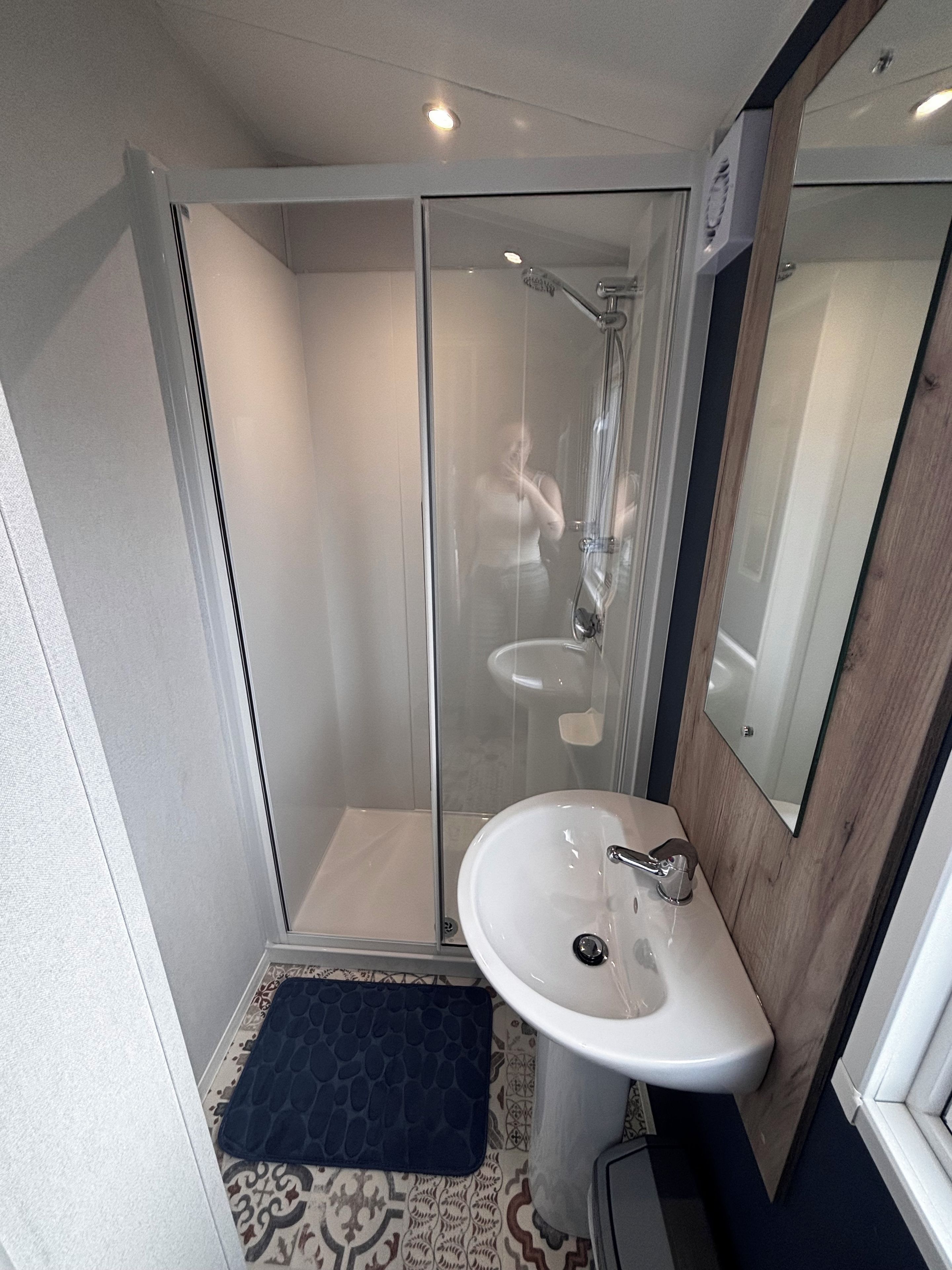 A bathroom with a glass-enclosed shower, a white sink, and a wooden-framed mirror.