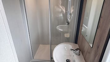 A bathroom with a glass-enclosed shower, a white sink, and a wooden-framed mirror.