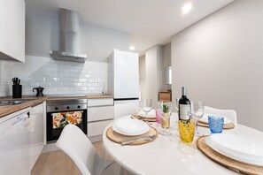 A modern kitchen with white appliances, a dining area with a table set for two, and a view into the adjacent living space. - MalagaSuite Urban Beach B (Torremolinos)