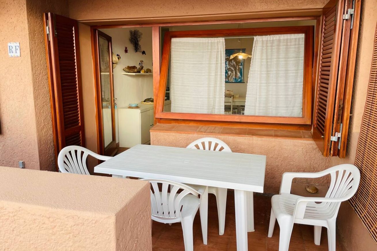 Une terrasse avec une table et des chaises blanches, une fenêtre avec des rideaux et une porte dotée d’un volet en bois.