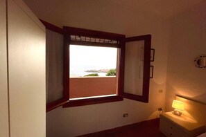 Une chambre avec une fenêtre donnant sur la plage, une lampe de chevet et un interrupteur fixé au mur.