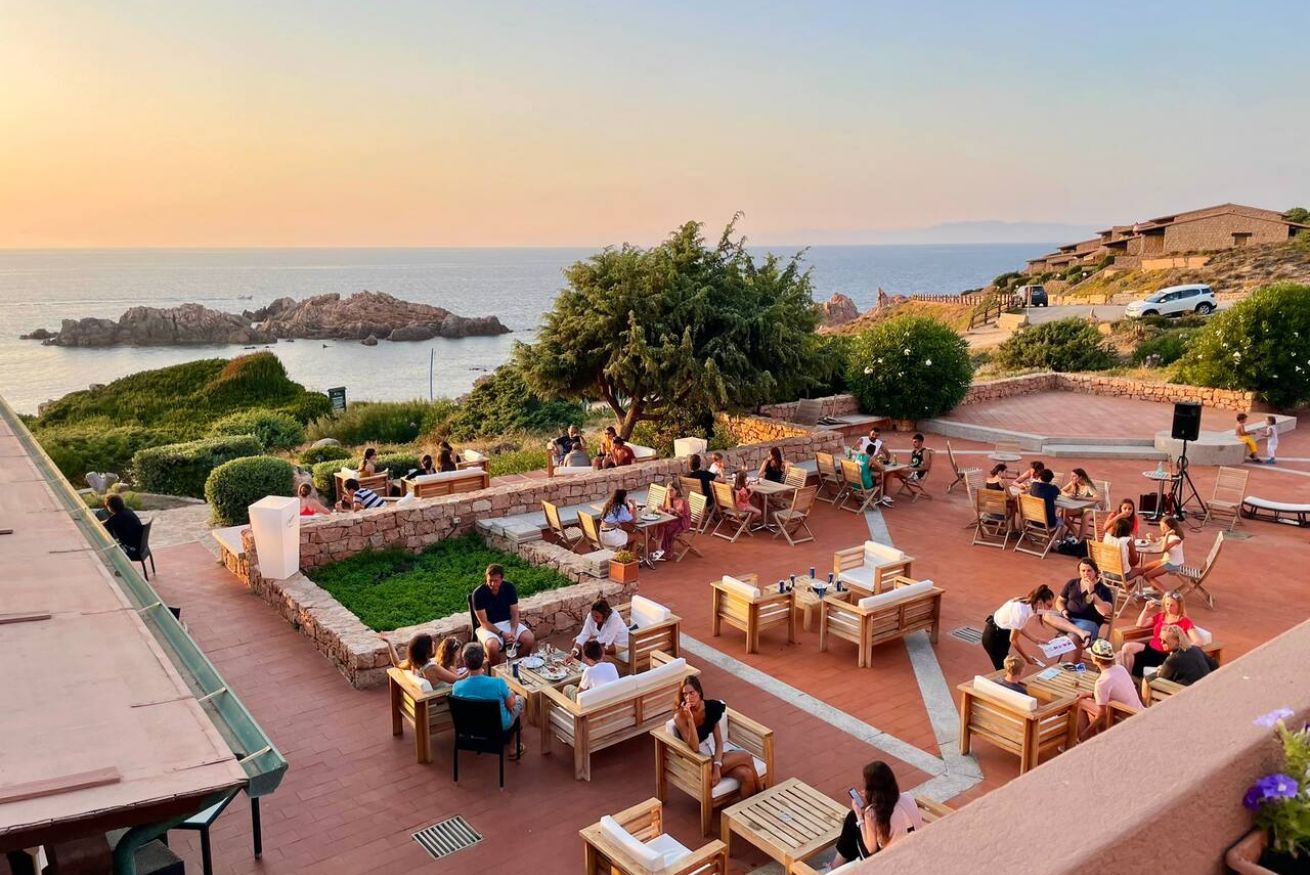 Un espacio al aire libre con mesas y sillas, con vistas a un paisaje costero con rocas y vegetación.