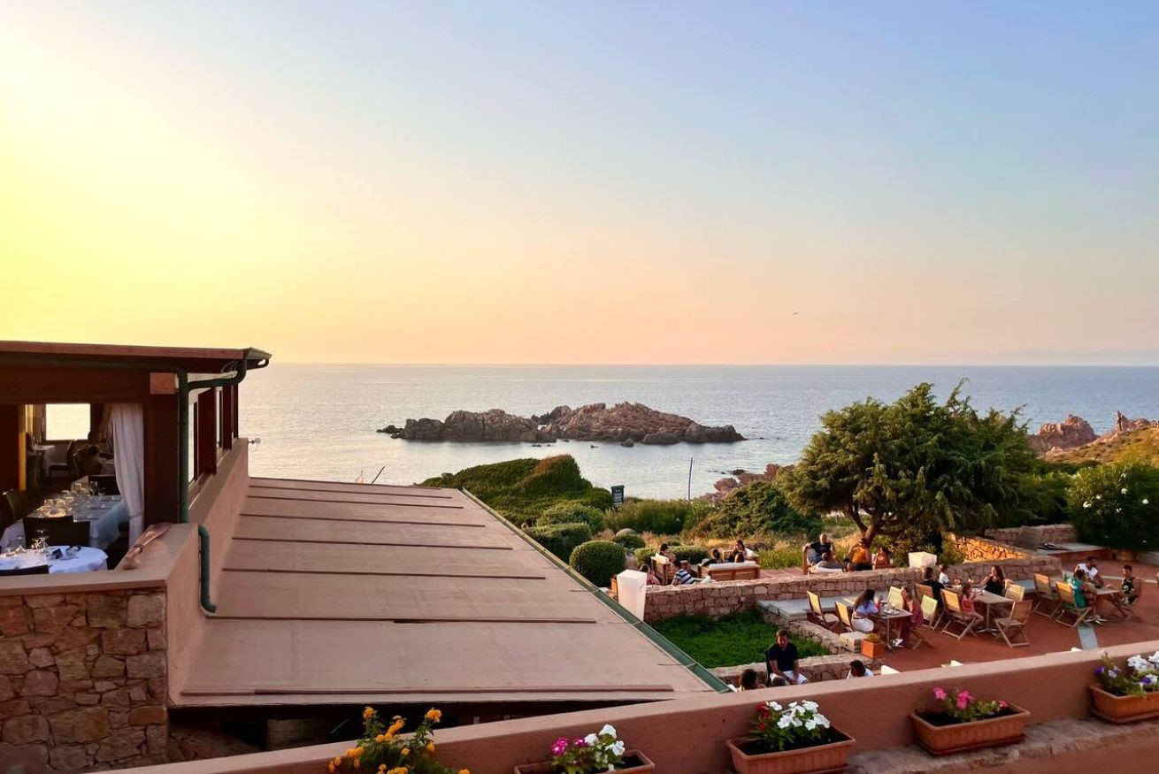 Una terraza con mobiliario exterior que ofrece vistas a un paisaje costero con afloramientos rocosos y el mar.
