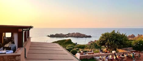 Una terraza con mobiliario exterior que ofrece vistas a un paisaje costero con afloramientos rocosos y el mar.