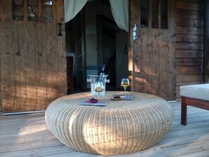 Un poggiapiedi rotondo in vimini su un pontile di legno, con una bottiglia e un bicchiere di vino sopra.