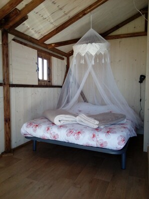 Een eenpersoonsbed met hemelbed in een kamer met houten wanden en een schuine plafond.